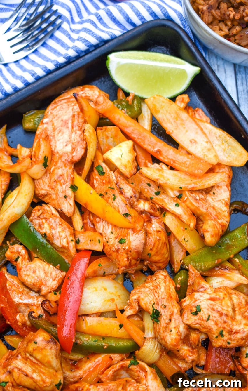 sheet pan chicken fajitas on a metal baking sheet with fresh lime edges on the side
