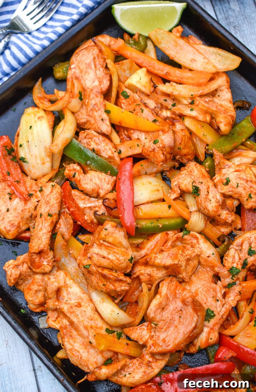 sheet pan chicken fajitas on a metal baking sheet with fresh lime edges on the side