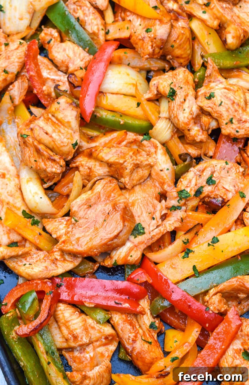 a close up of chicken and sliced veggies in fajita seasoning on a metal sheet pan