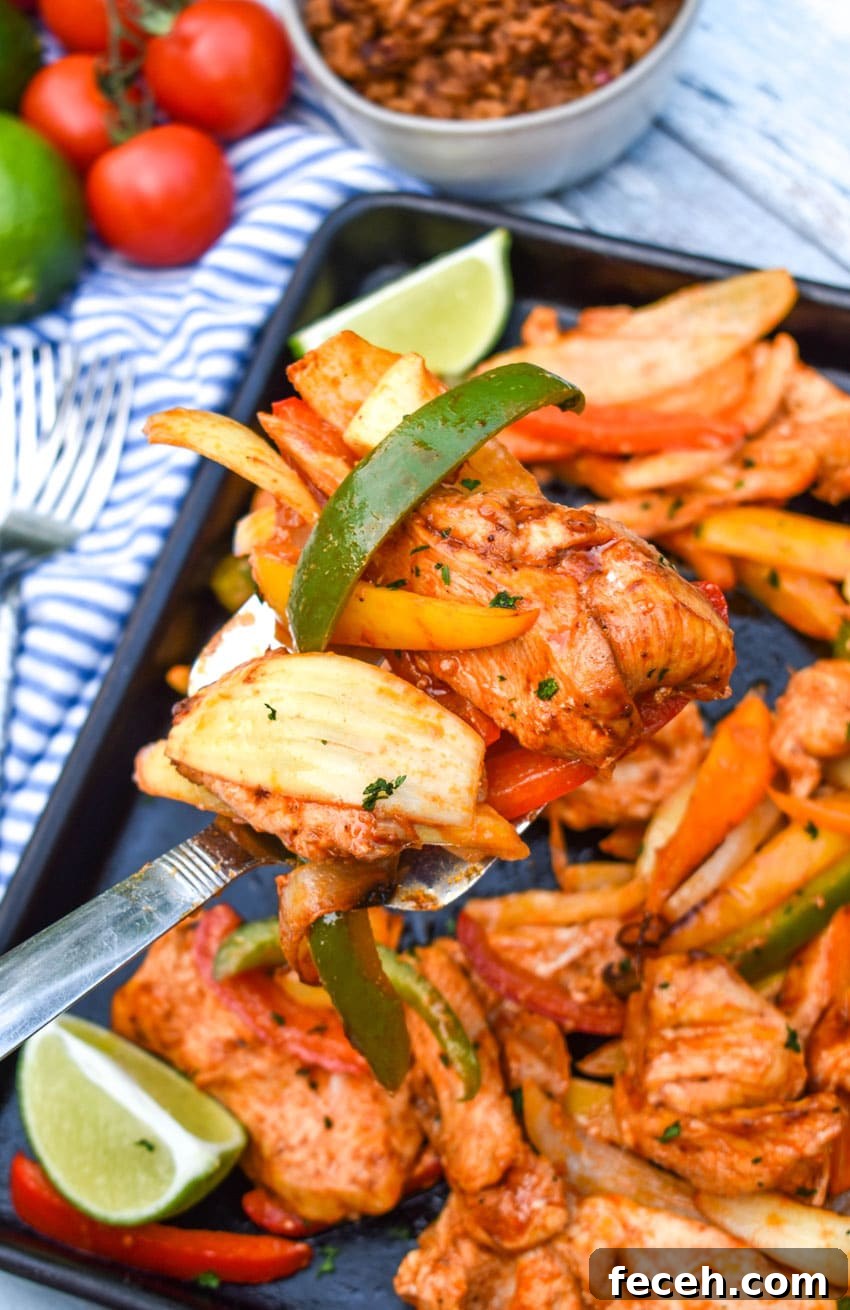 a silver spatula scooping chicken and vegetable fajita mixture off of a metal sheet pan