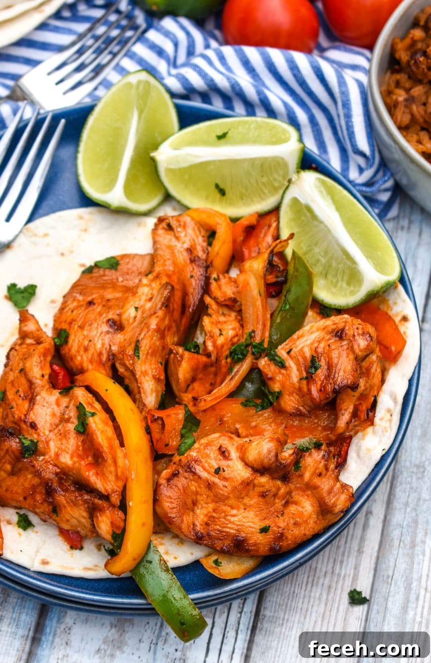 sheet pan chicken fajitas mixture on flour tortillas on a blue plate with fresh lime wedges on the side