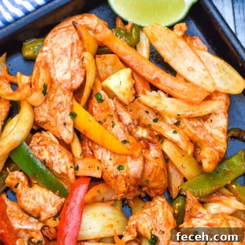 sheet pan chicken fajitas on a metal baking sheet with fresh lime edges on the side