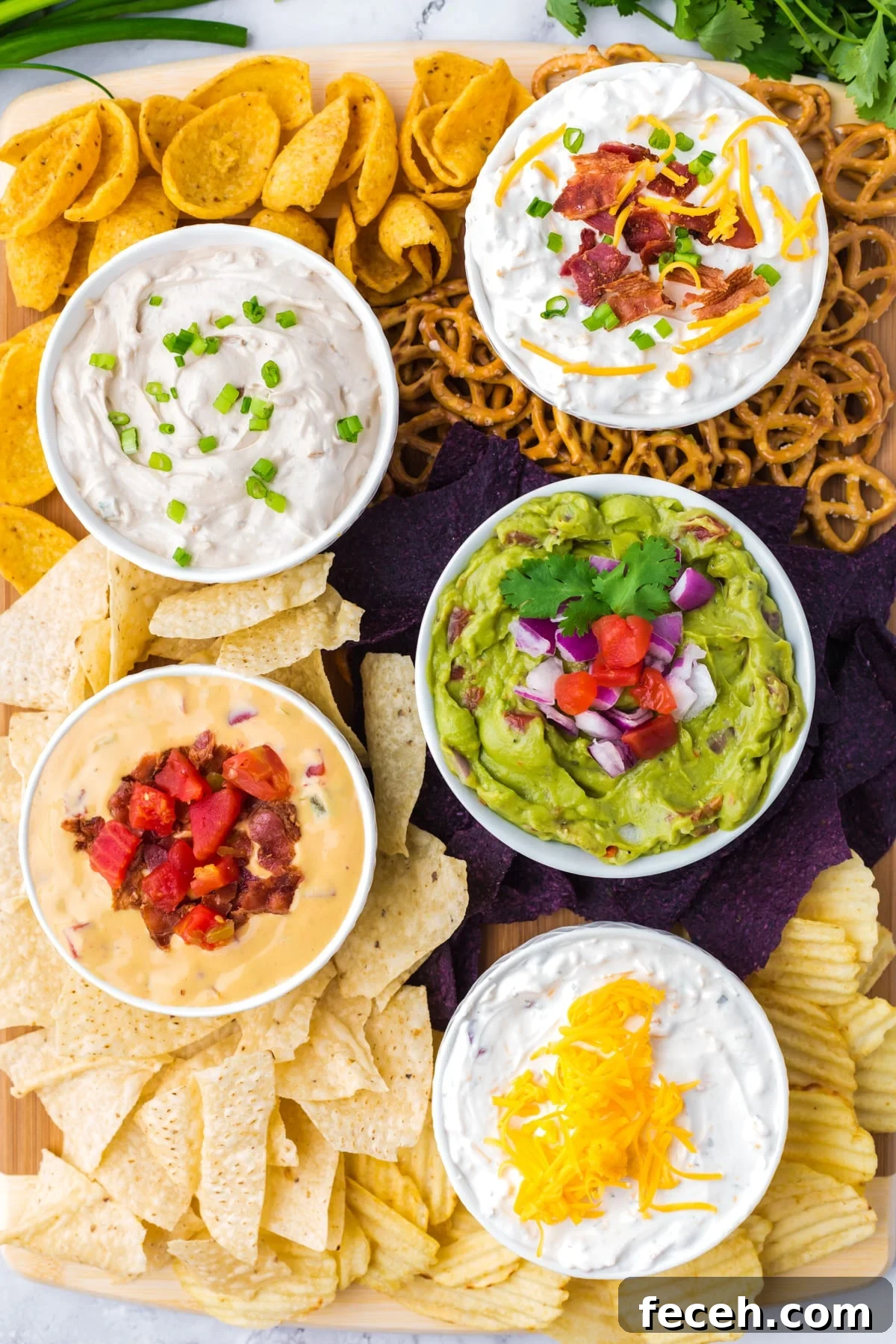 Five small bowls filled with dip, surrounded by various types of chips on a wooden board.