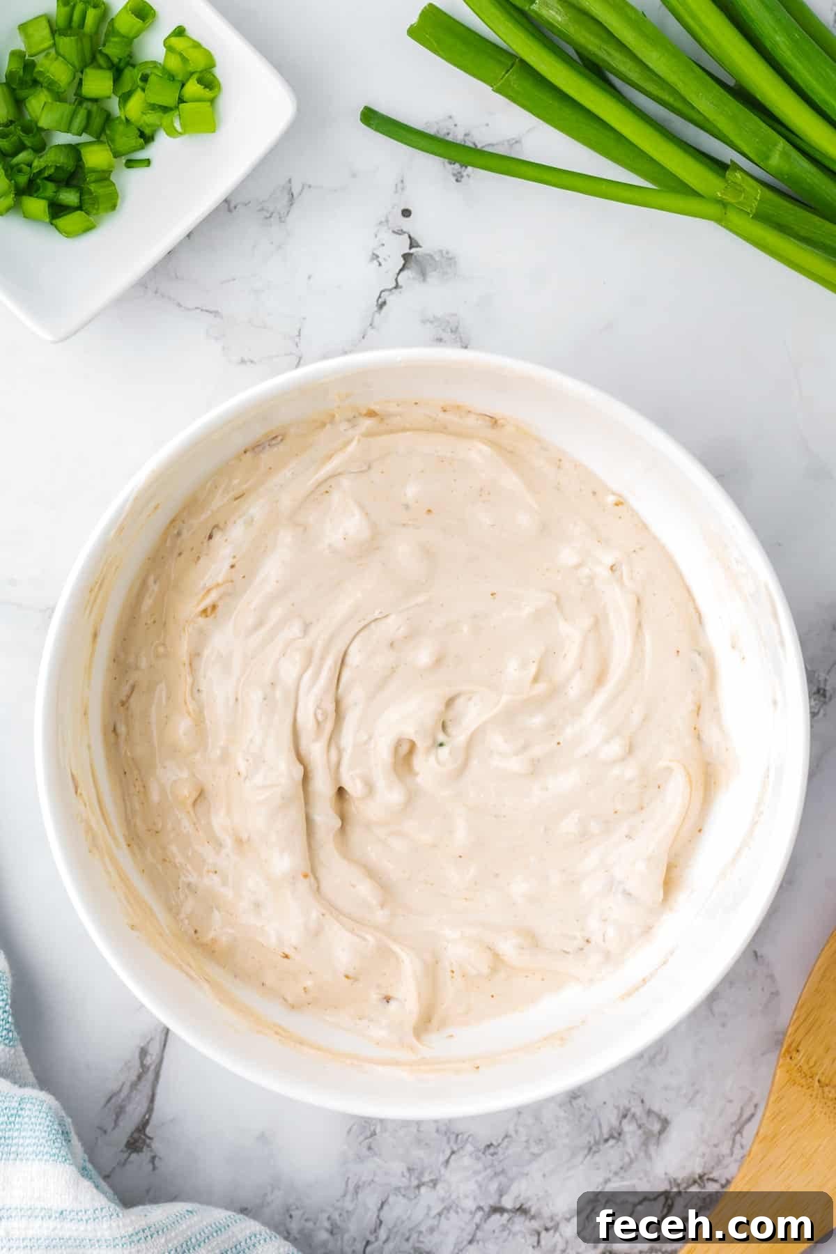 A bowl of onion dip, with green onions around the edges.