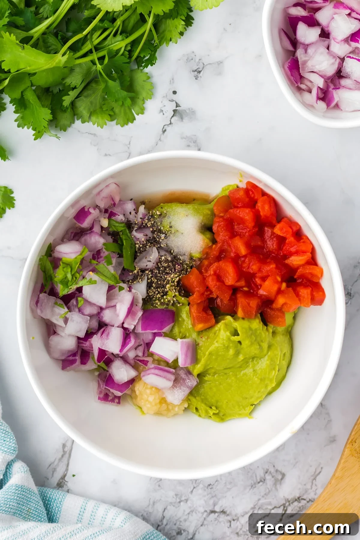 A bowl of mashed avocado topped with red onion, tomato, garlic, pepper, salt, and cilantro.