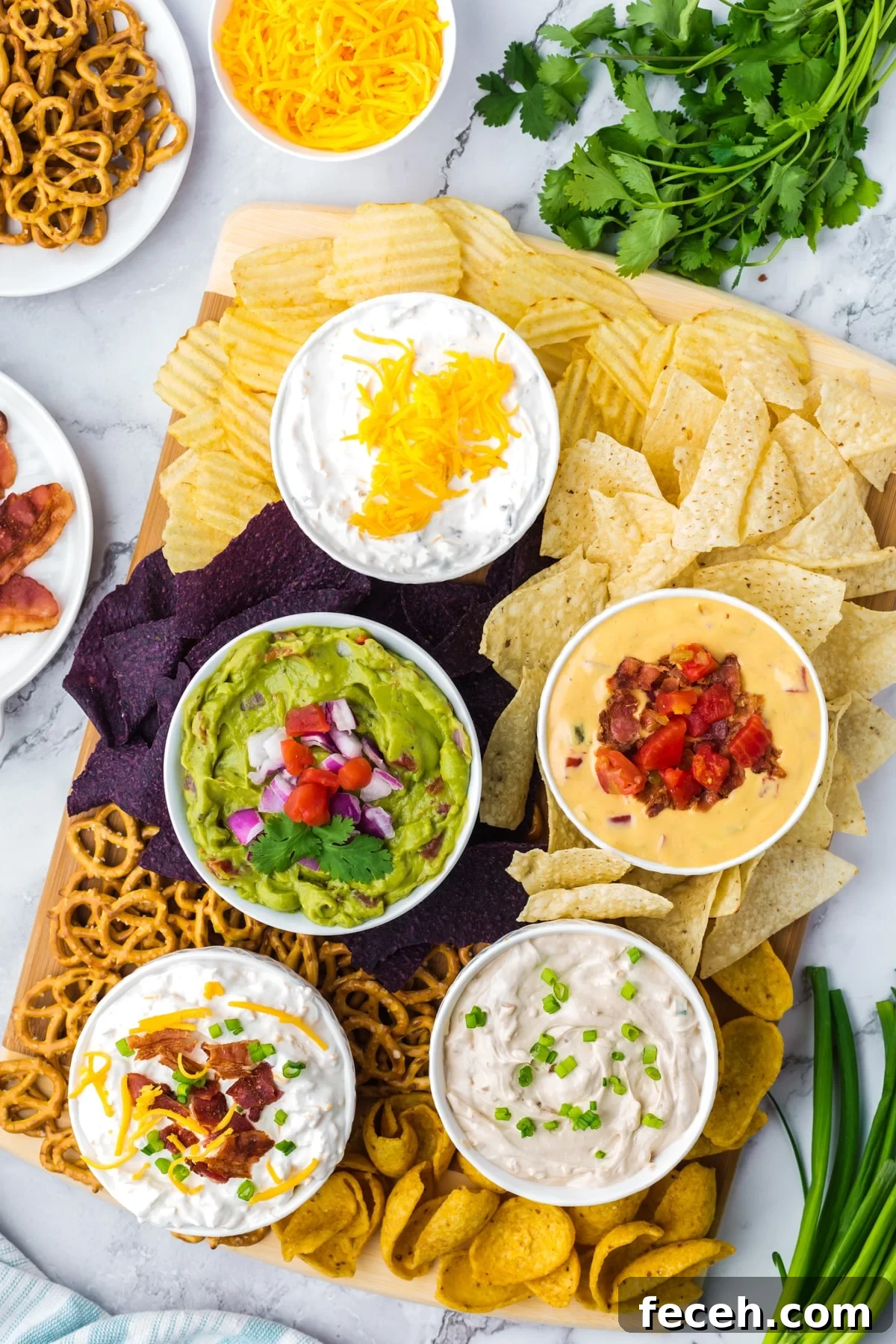 A board with five different dips with various chips arranged on a board below.