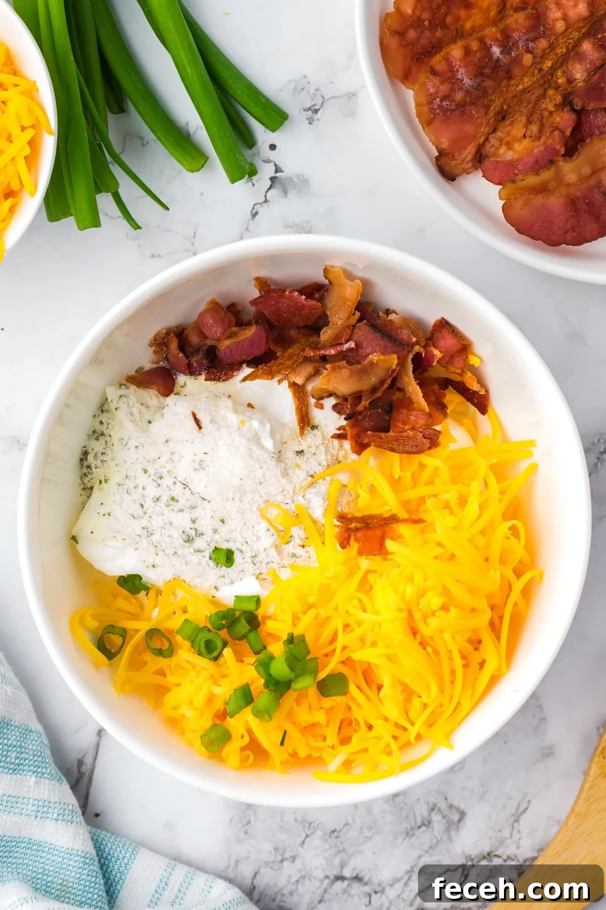 A white bowl featuring shredded cheese, bacon, ranch, and green onions.