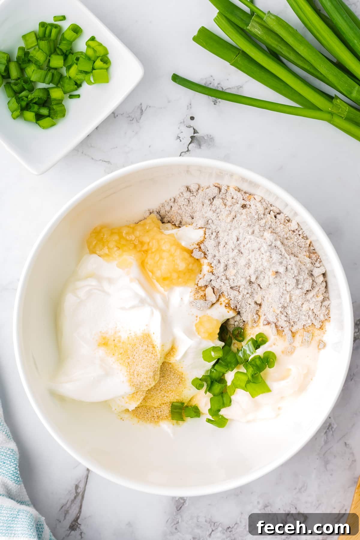 A white bowl filled with sour cream, onion mix, garlic, green onions, etc.
