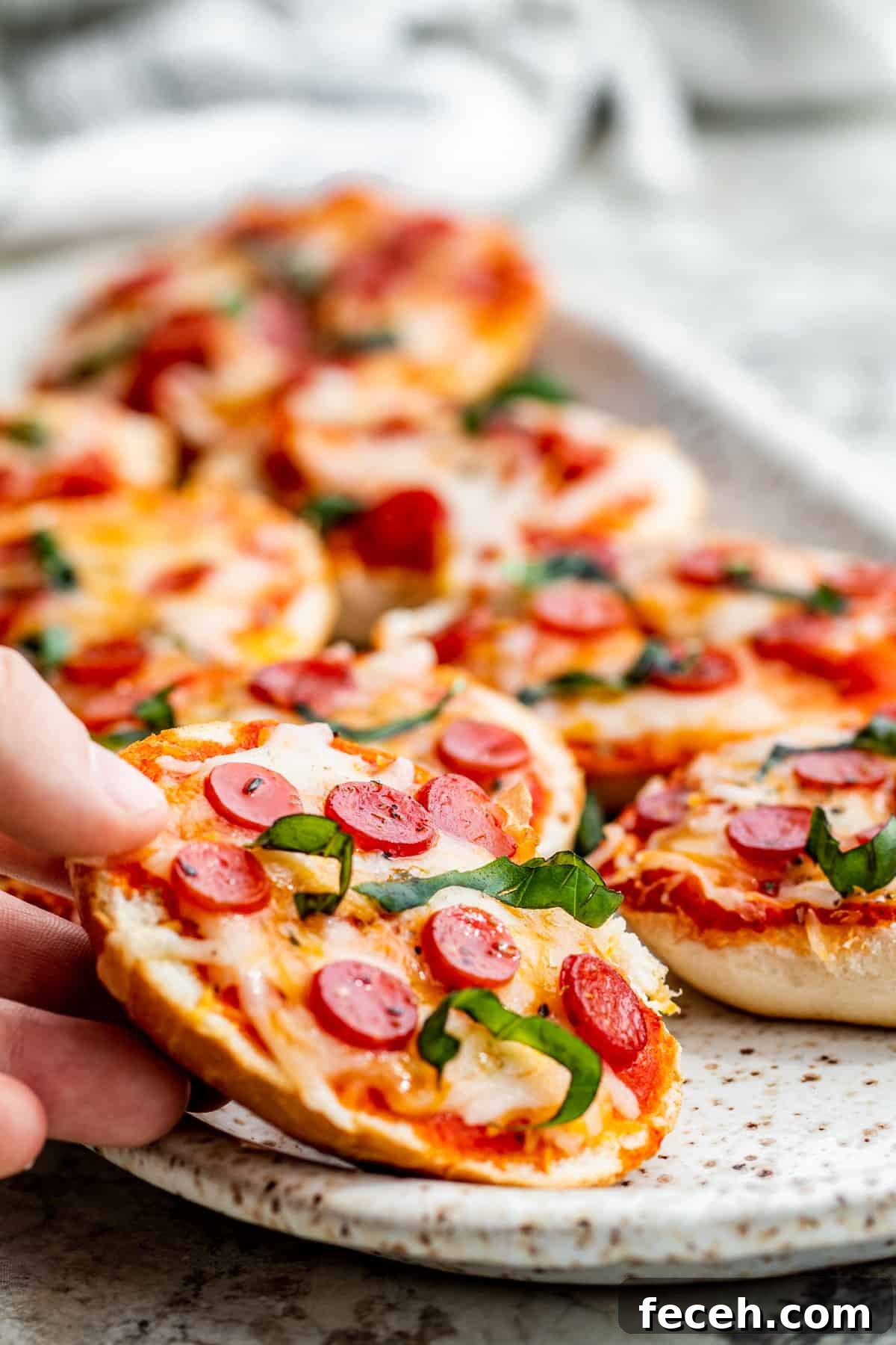 Hand picking up pizza bagel.