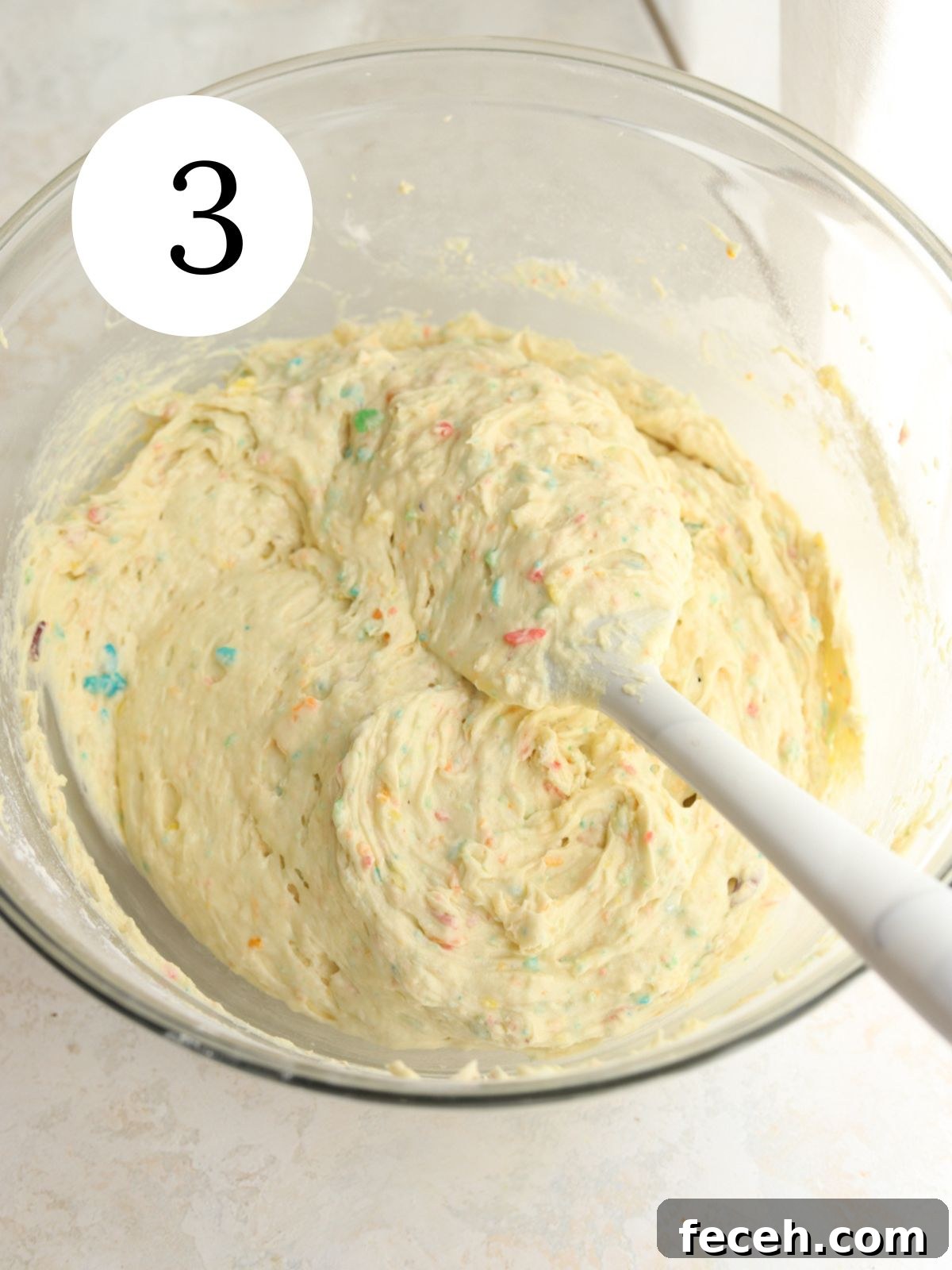 Cake batter in a glass mixing bowl with a spatula in it.