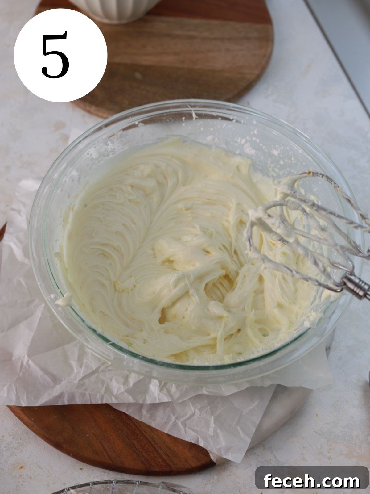 A large glass bowl with frosting next to an electric mixer.