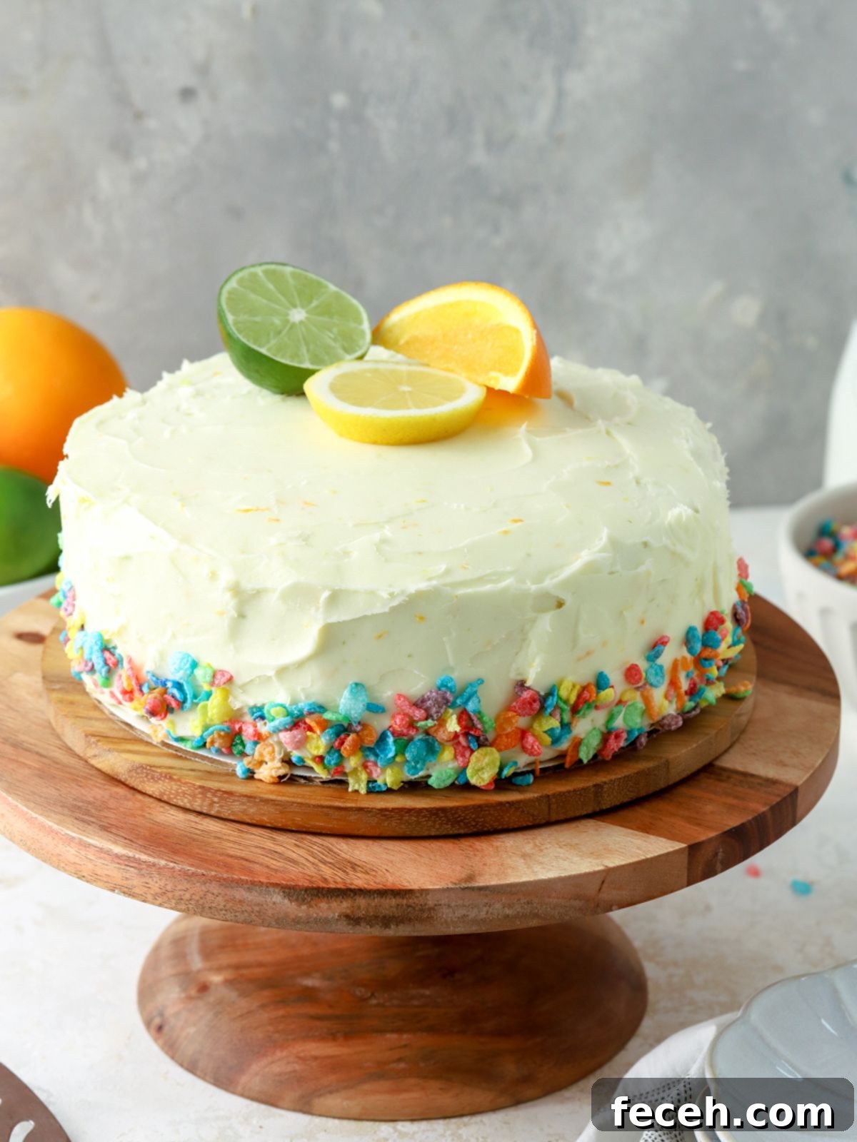 A frosted cake decorated with fruity pebbles and fruit on a cake stand.