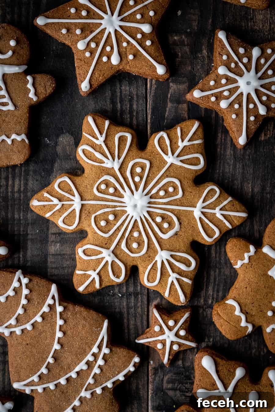 close up of a vegan gingerbread snowflake cookie with white icing on a dark wood background.
