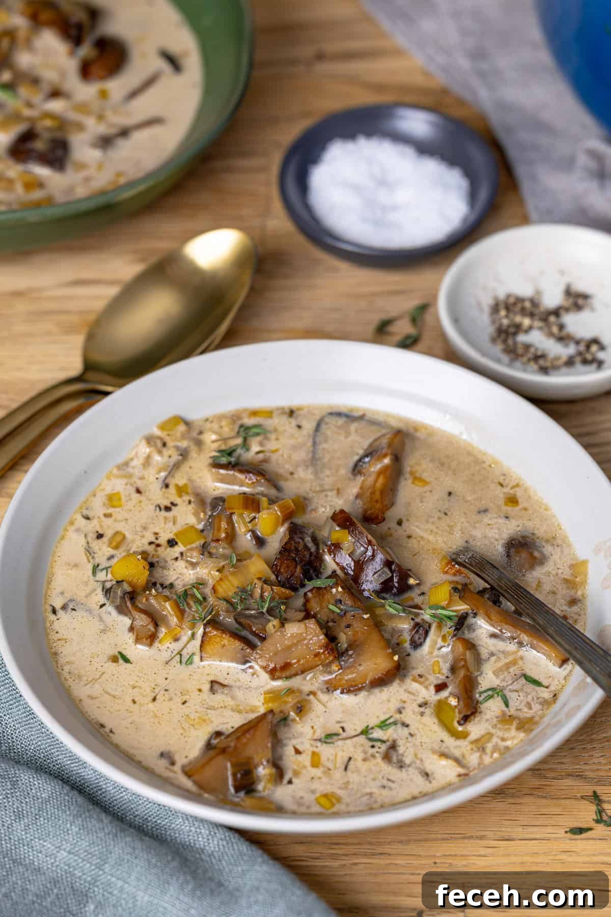 A close up of a white bowl with mushroom and leek soup on a butcherblock table.