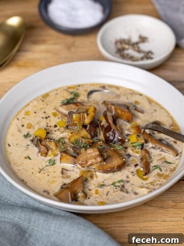 A close up of a white bowl with mushroom and leek soup on a butcherblock table.