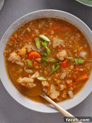A bowl of cauliflower and lentil soup topped with scallions on a gray table.