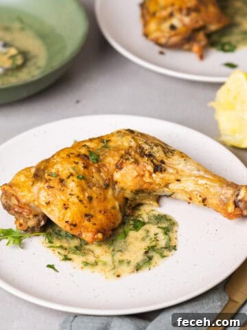 A serving of golden brown roasted chicken leg quarters with an herb sauce on a gray table.