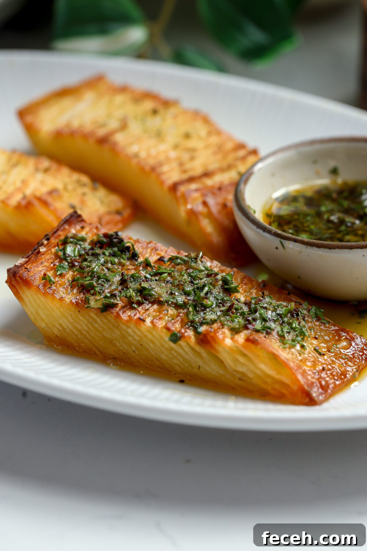 Three golden-brown, crispy stacks garnished with a green chive oil. A small bowl of buttery dipping sauce is beside them.