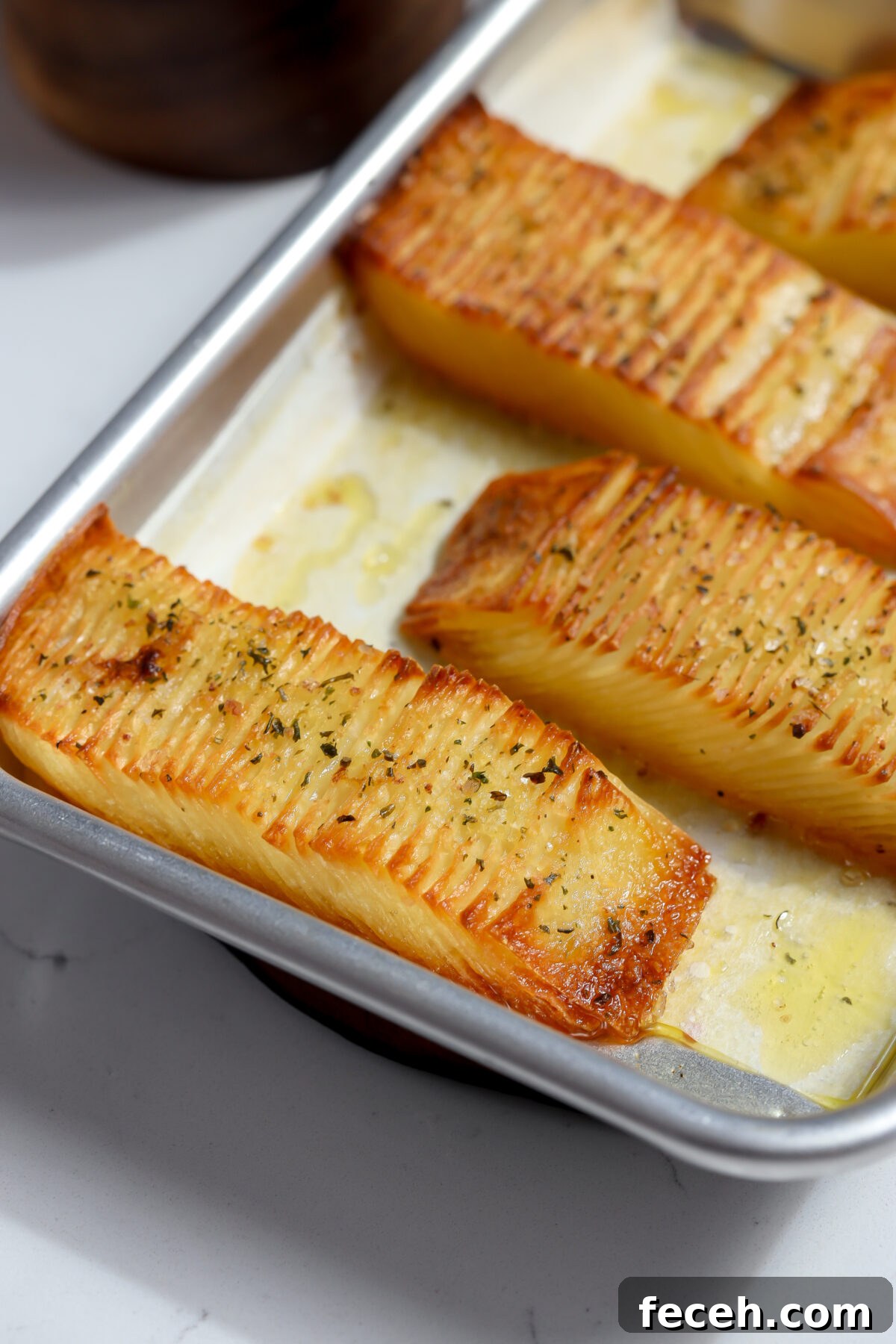 A baking tray with golden-brown rows of crispy potato stacks, seasoned with herbs and olive oil. The potato stacks are sliced thinly and roasted to perfection, showcasing a deliciously textured and appetizing appearance.