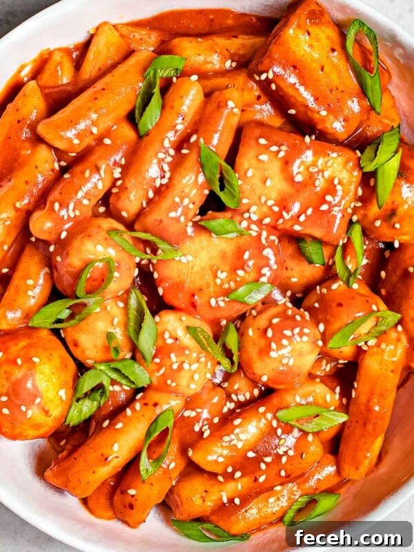 tteokbokki with fish cakes and eggs garnished with sesame seeds and scallions in a white bowl