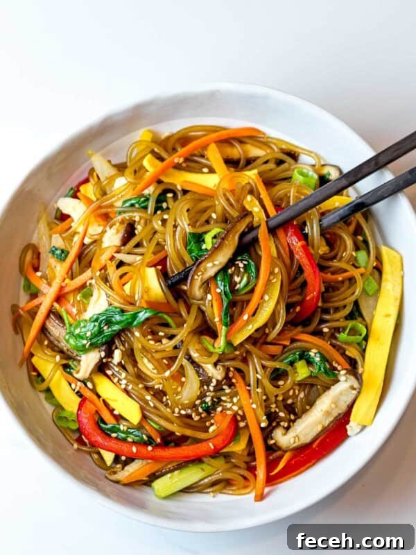 japchae noodles with red peppers, carrots, and shiitake mushrooms in a white bowl with chopsticks