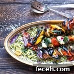 Grilled Veggie and Halloumi Skewers with Lemon Herb Marinade 4 Serving plate with zoodles and grilled veggies skewers, with a serving spoon and fork.