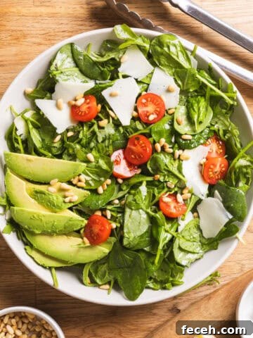 A serving bowl of spinach and arugula salad with a lemon thyme vinaigrette on a butcherblock countertop.