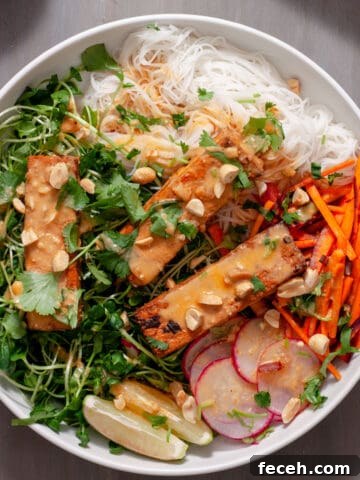 A white bowl with a summer roll salad topped with crispy peanut tofu, herbs, peanuts and peanut sauce.