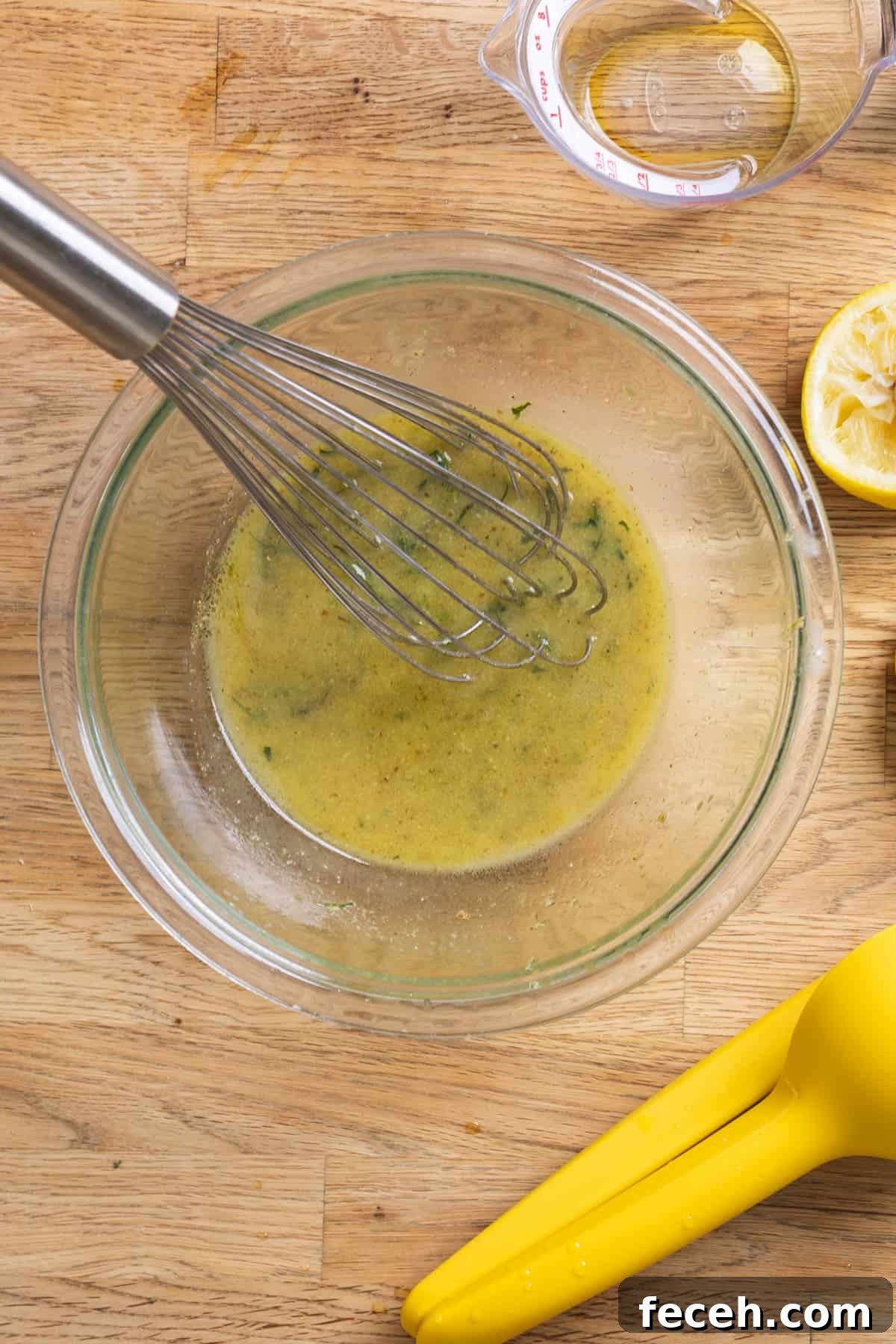 Lemon Dijon Dressing getting whisked together in a glass bowl on a butcherblock counter.