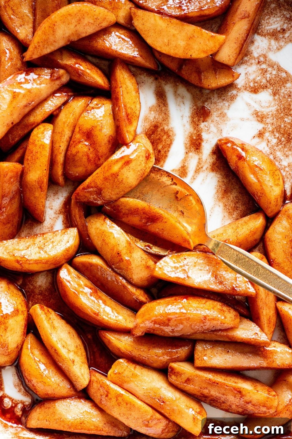 Close up of a white ceramic baking dish filled with paleo baked cinnamon apples with a gold spoon scooping them.