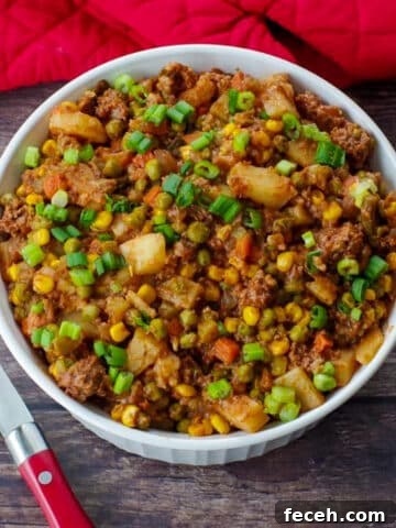 shipwreck casserole on a wooden surface with red oven mitts in background and spoon to the right.
