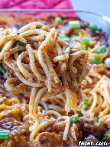 Million Dollar Spaghetti Casserole being held up on a spoon over glass casserole dish