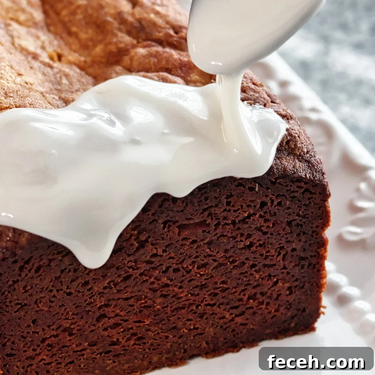 pouring thick white glaze over top and down sides of lemon loaf cake.