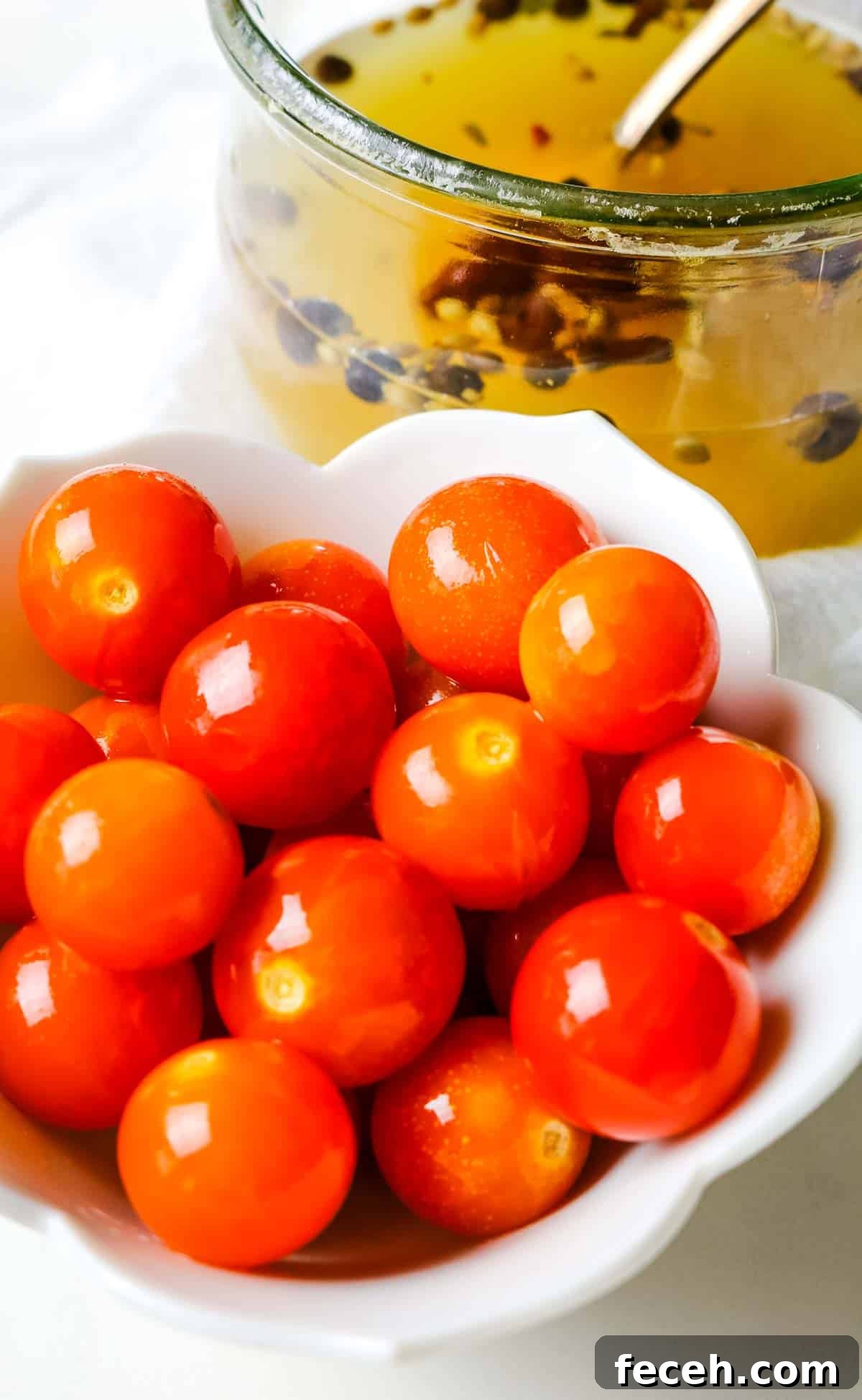fermented cherry tomatoes in a small white dish with brine in jar in background.