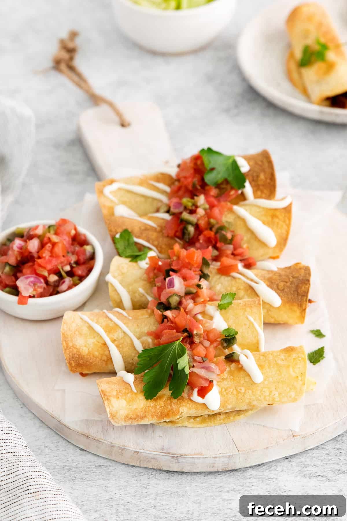 Taquitos topped with pico de gallo on a cutting board.