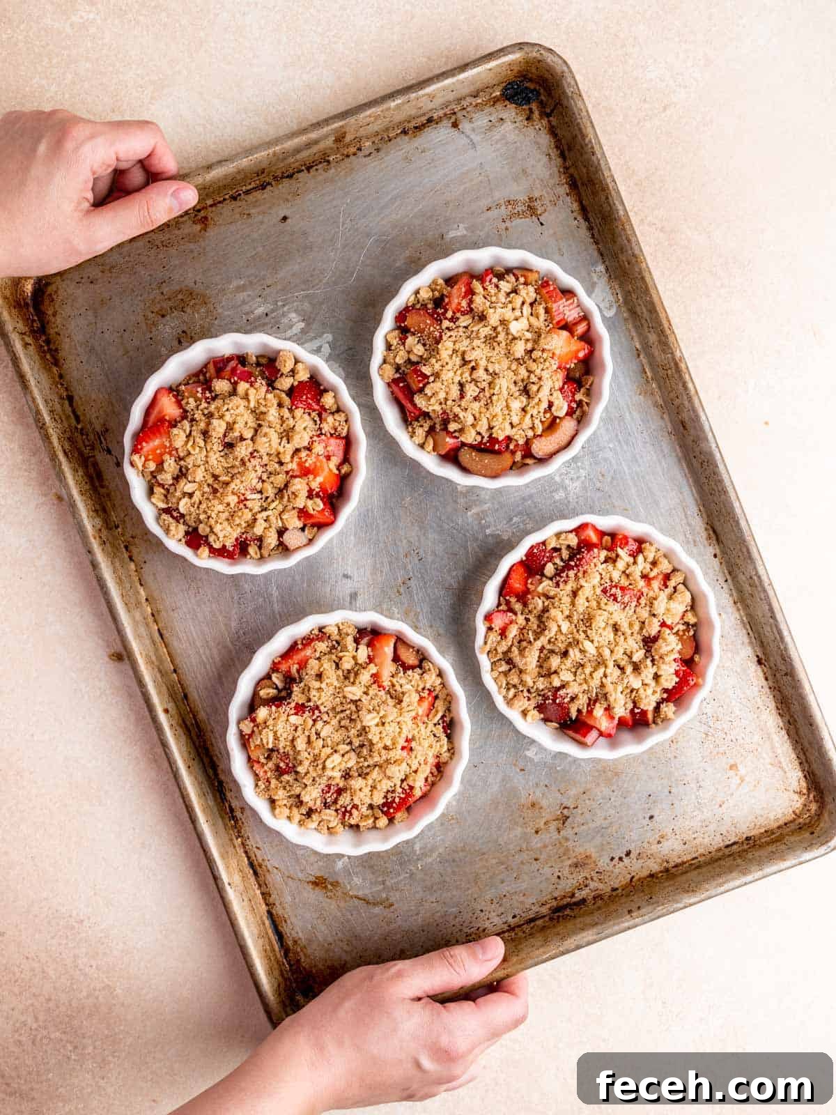 Ramekins of strawberry rhubarb crisp on a baking sheet.