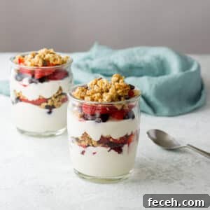 Two jars filled with layered yogurt, fruit and granola with a napkin in the background - square