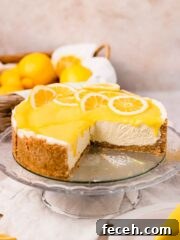 lemon curd cheesecake on glass cake stand topped with lemon curd with a wedge cut out