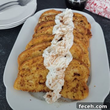 EggNog French Toast with eggnog whipped cream on a white platter next to plates