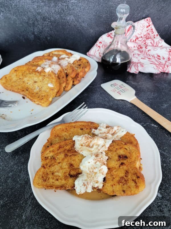 Eggnog French Toast slices on a white plate garnished with eggnog whipped cream and cinnamon/nutmeg next to a platter and a spatula