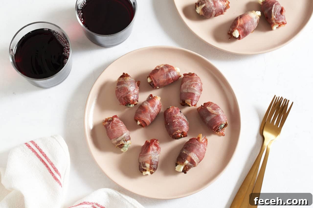 Prosciutto-Wrapped Dates with Goat Cheese and Honey Drizzle 2 Two pink plates of prosciutto wrapped dates, gold forks are on the right, two glasses of red wine are in the upper left.