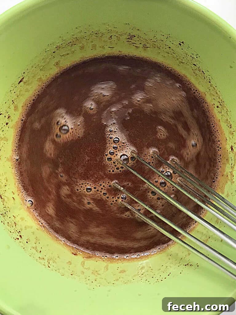 Green bowl with chocolate custard mixture and whisk.