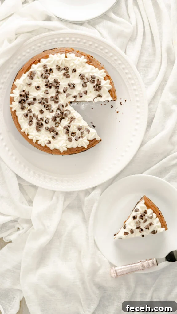 Top view of instant pot cheesecake with slice of cheesecake on white plate on white fabric background.