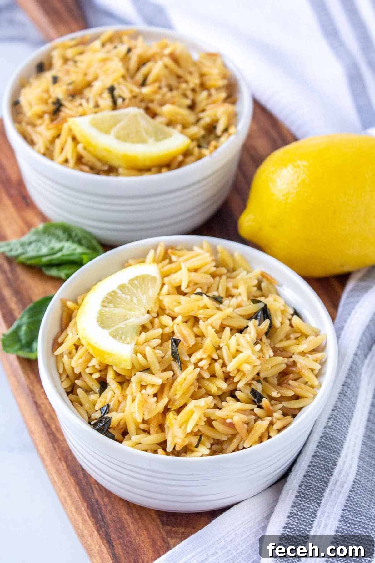 Two ramekins filled with lemon parmesan orzo topped with a half lemon slice.
