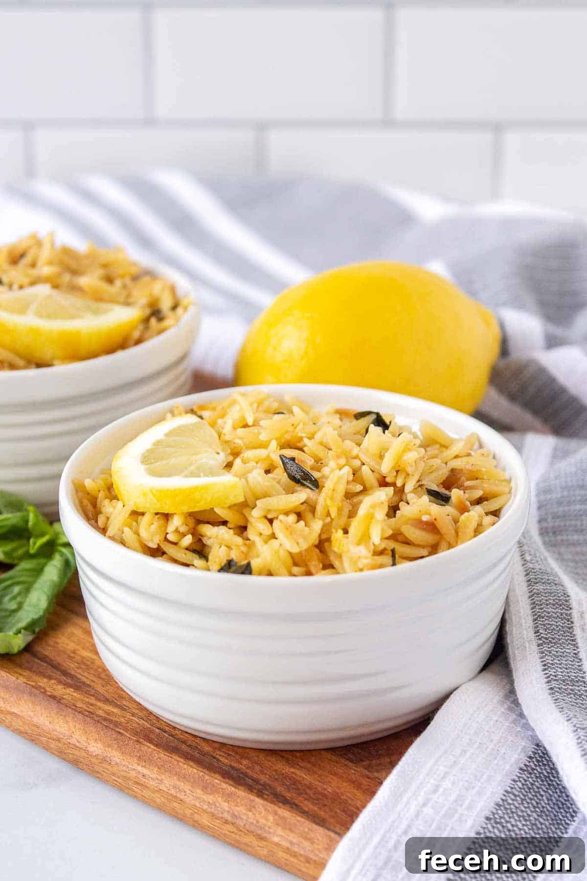 Ramekins filled with lemon parmesan orzo topped with a half lemon slice. There is fresh basil and lemon in the background.