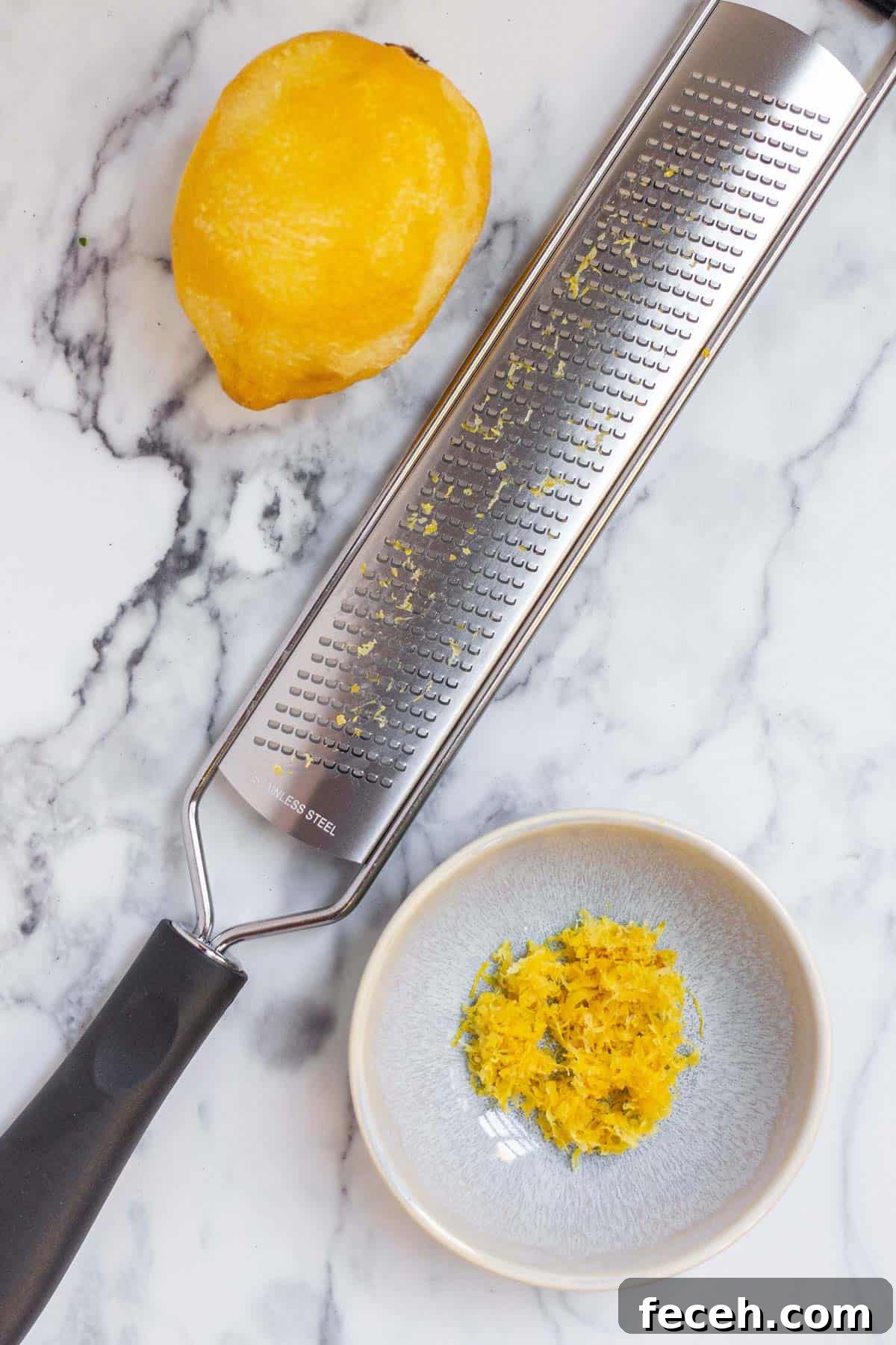 A small pinch bowl filled with fresh lemon zest next to a whole lemon and a microplane zester.