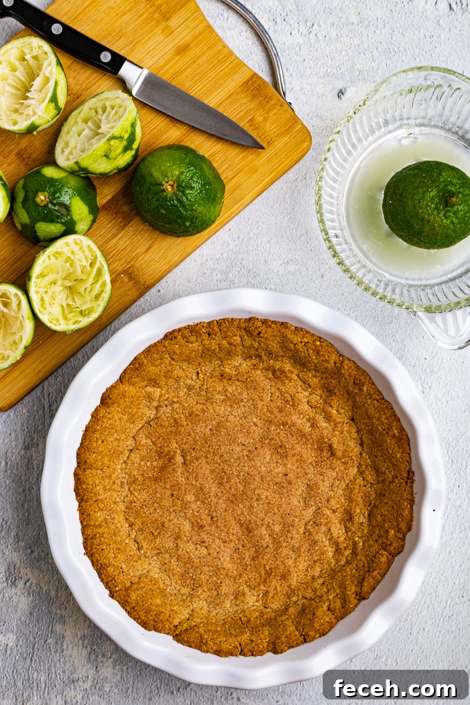 Overhead shot of gluten free graham cracker crust in a pie plate, with squeezed limes in the background.