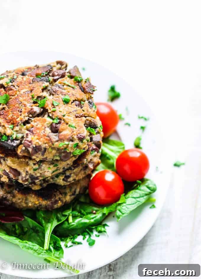 Stock of homemade veggie burgers on a white plate on white board, with spinach and tomatoes on a side