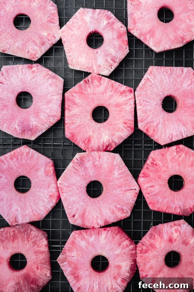 Pink pineapple rings arranged on a wire rack before drying — vibrant pink, juicy, and fresh.