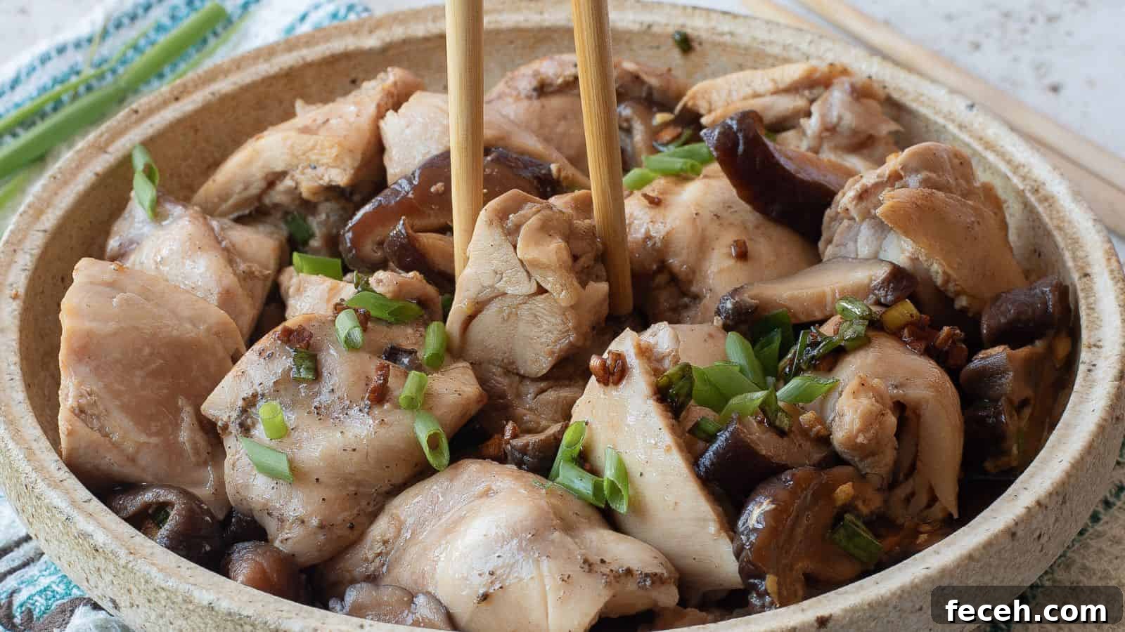 31 Asian Weeknight Dinners to Make Mealtime Exciting 12 A bowl of steamed chicken pieces with mushrooms, garnished with chopped green onions, with chopsticks picking up a piece.